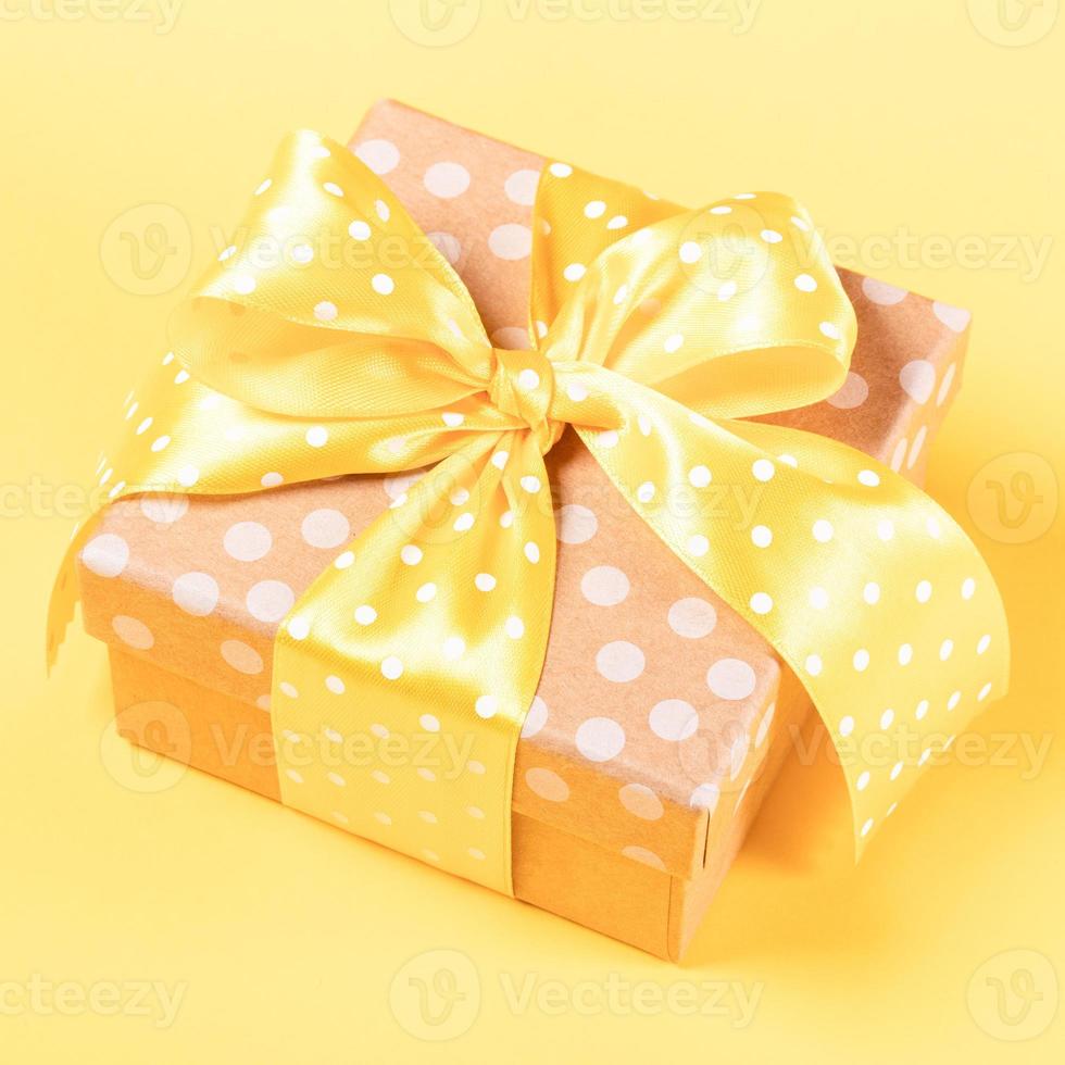 coffret cadeau enveloppé de papier kraft à pois avec noeud à pois jaune sur gros plan jaune. photo