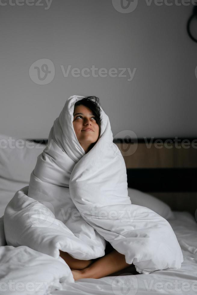 femme paresseuse enveloppée dans une couverture douce assise dans un lit douillet photo