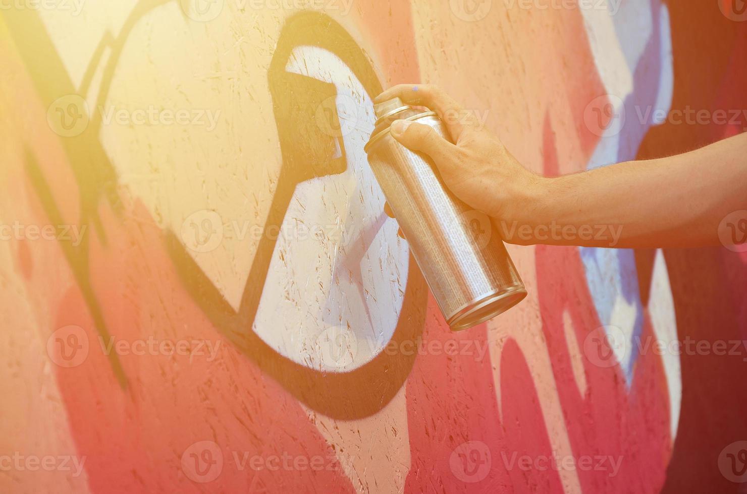 une main avec une bombe aérosol qui dessine un nouveau graffiti sur le mur. photo du processus de dessin d'un graffiti sur un gros plan de mur en bois. le concept d'art de rue et de vandalisme illégal