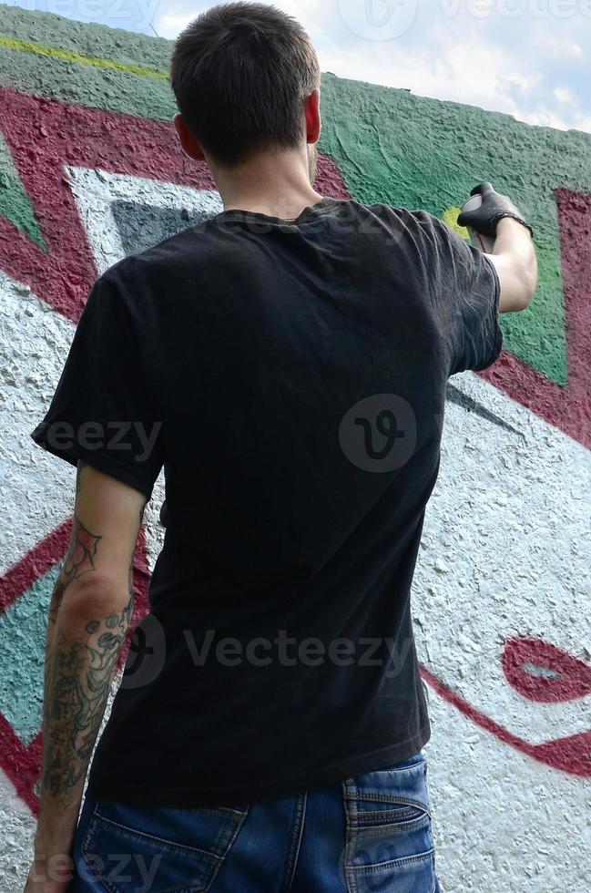 un jeune hooligan peint des graffitis sur un mur de béton. concept de vandalisme illégal. art de rue photo