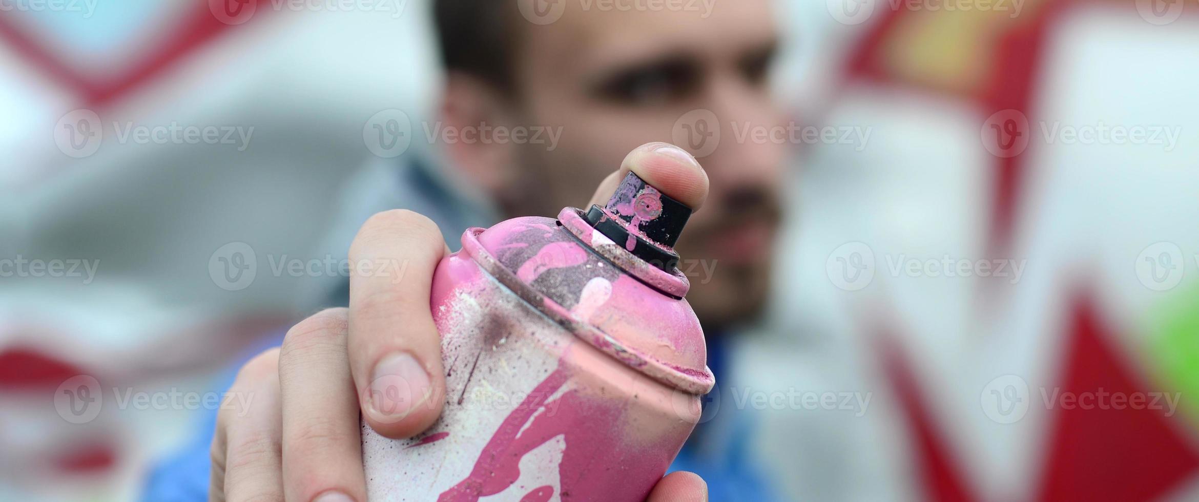 un jeune graffeur en veste bleue tient devant lui un pot de peinture sur fond de graffitis colorés. concept d'art de rue et de vandalisme photo