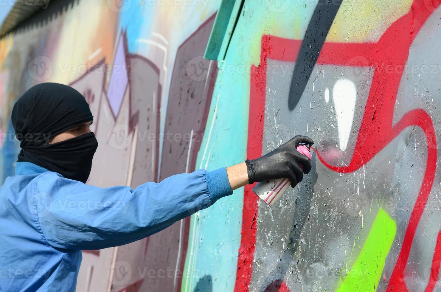 un jeune hooligan au visage caché peint des graffitis sur un mur métallique. concept de vandalisme illégal photo