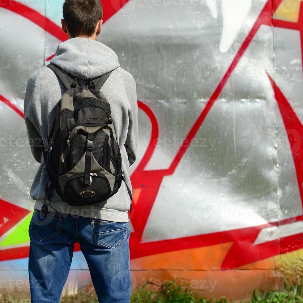 un jeune graffeur avec un sac noir regarde le mur avec son graffiti sur un mur. notion d'art de rue photo