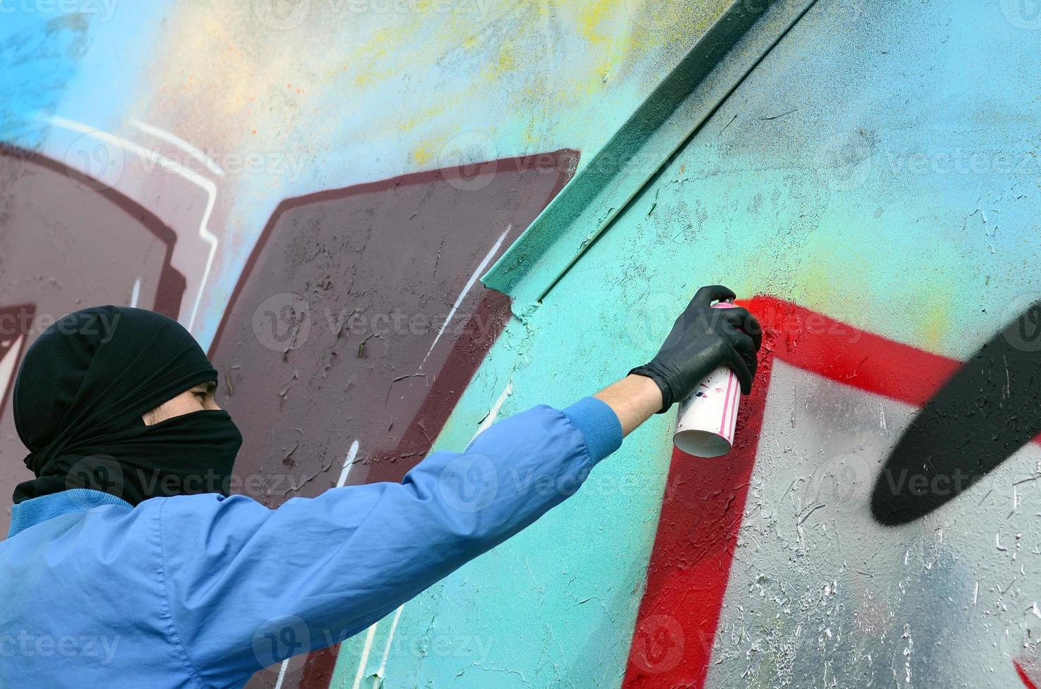 un jeune hooligan au visage caché peint des graffitis sur un mur métallique. concept de vandalisme illégal photo