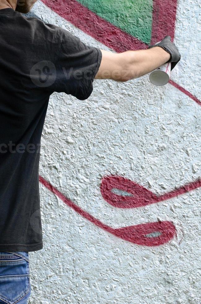 un jeune hooligan peint des graffitis sur un mur de béton. concept de vandalisme illégal. art de rue photo