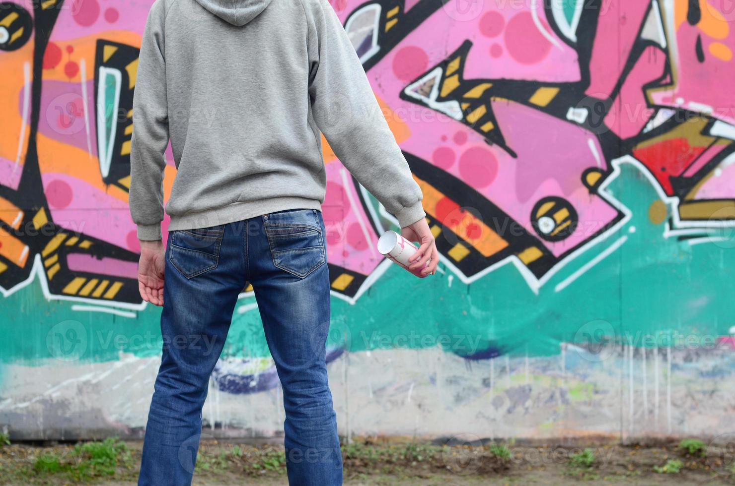 un jeune graffeur dans un sweat à capuche gris regarde le mur avec photo
