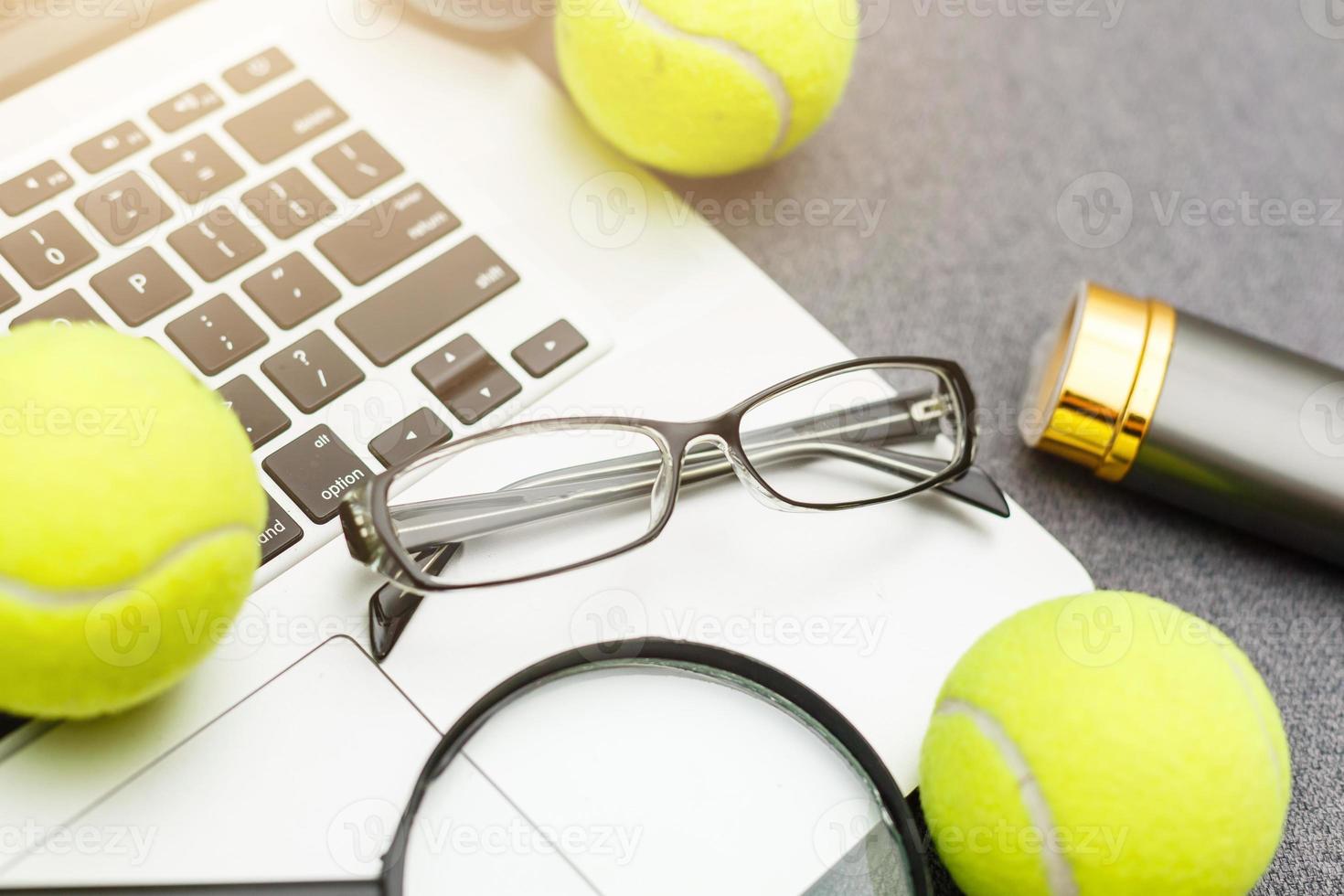 vue de dessus de l'ordinateur portable, de l'équipement sportif, de la balle de tennis, du volant, des lunettes sur la table grise de l'administration sportive. concept d'entreprise. photo