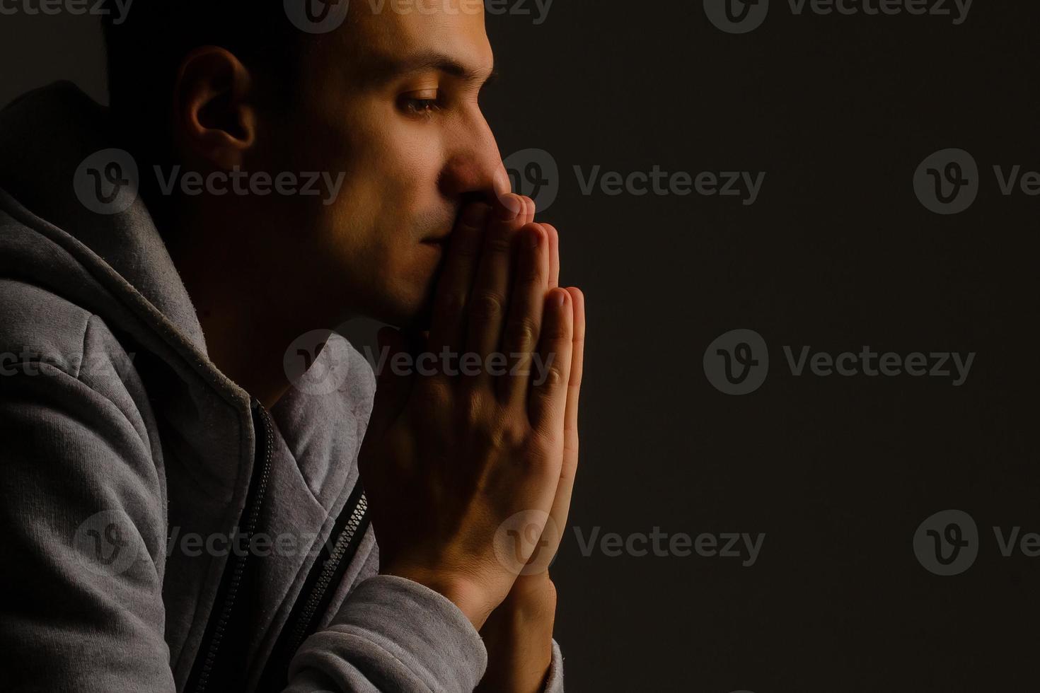 jeune homme religieux priant Dieu sur fond sombre, effet noir et blanc photo