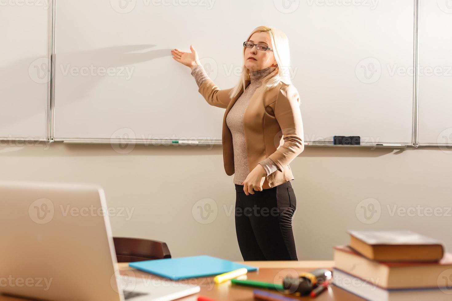 portrait d'une jolie enseignante tenant des blocs-notes dans une salle de classe à l'école photo