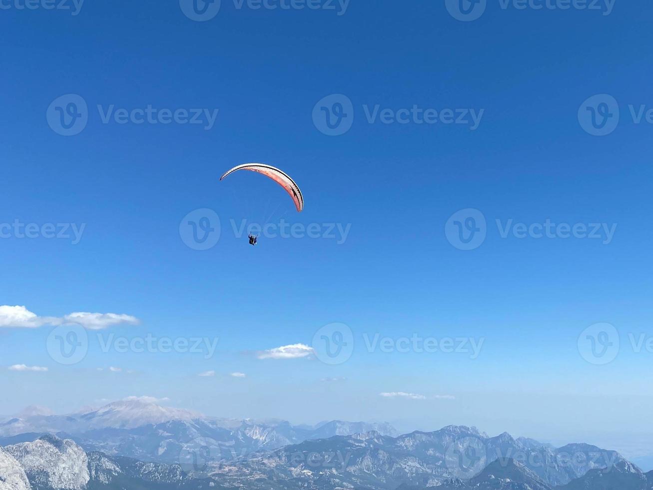 l'homme en parapente vole dans les airs à l'aide d'un parachute au-dessus des montagnes derrière le ciel bleu. sports extrêmes et liberté photo