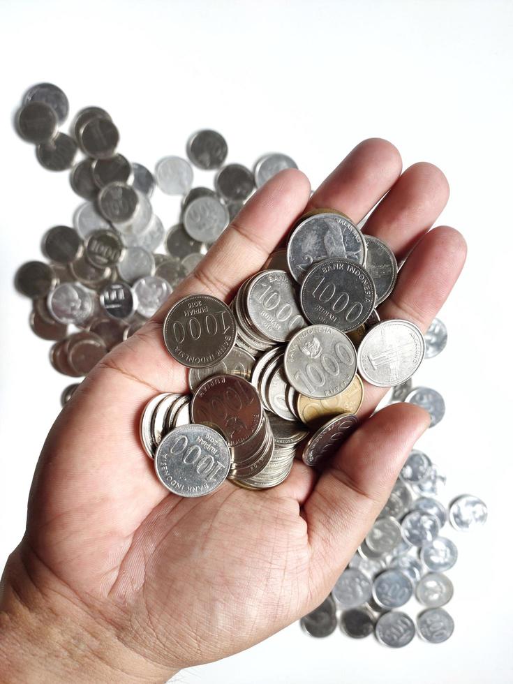 la collection de pièces de monnaie en roupie indonésienne sur la paume et il y a des pièces éparpillées derrière la paume. isolé sur fond blanc. vue de dessus photo