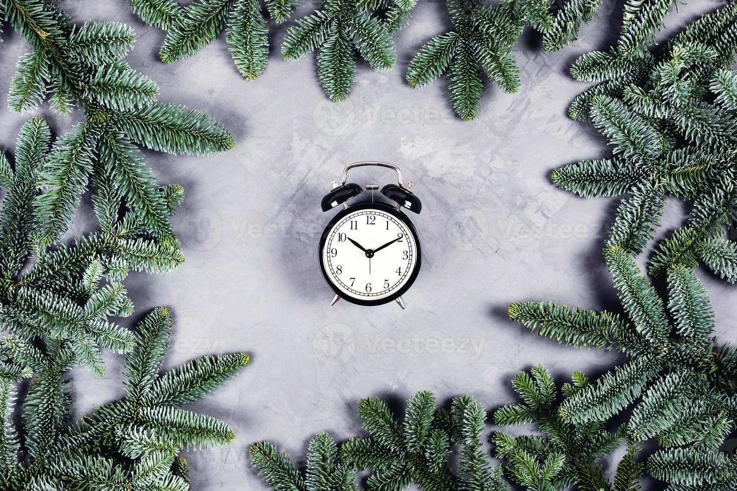 horloge noire sur fond de béton gris entouré de branches de noël. photo