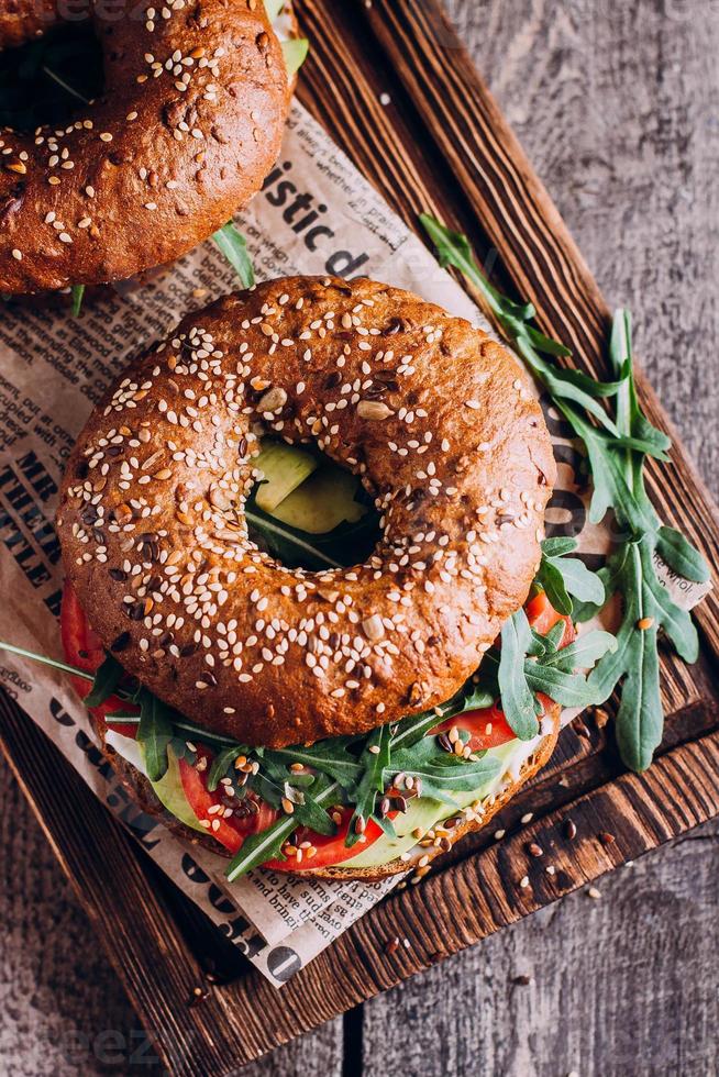 bagels à la crème, avocat, tomates et roquette sur planche de bois. petit-déjeuner sain. vue de dessus photo