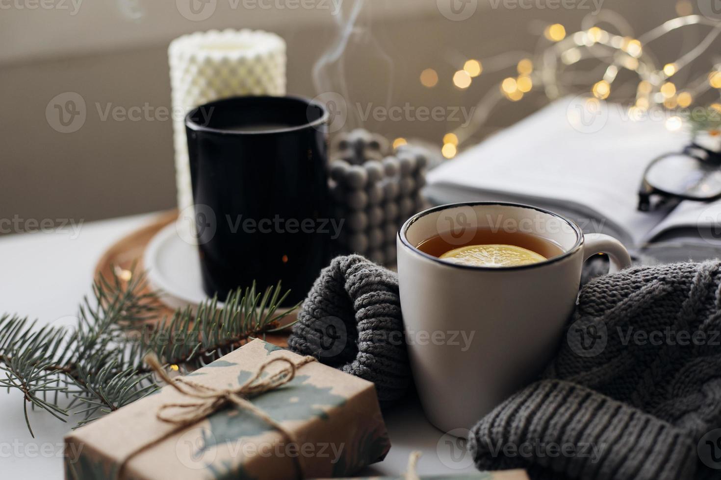 concept confortable de maison d'hiver. mug avec thé au citron, livre ouvert, pull chaud, bougies et sapin. bien-être, concept relaxant photo