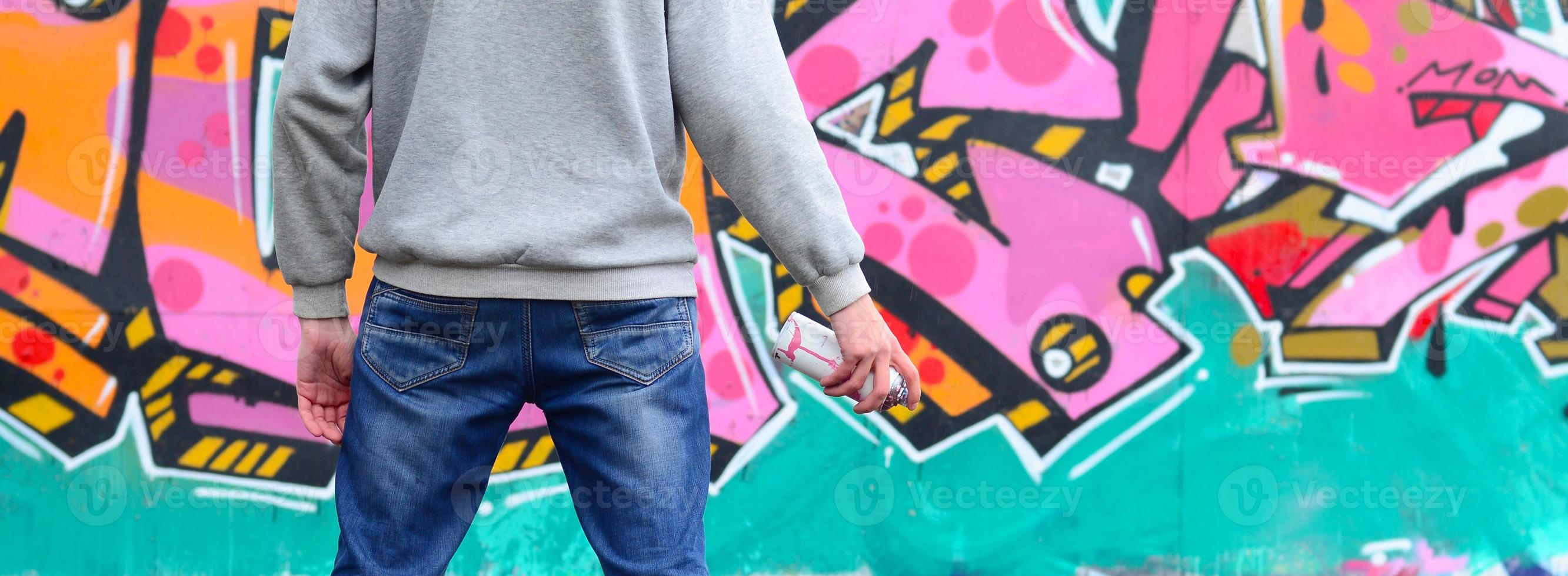 un jeune graffeur dans un sweat à capuche gris regarde le mur avec photo