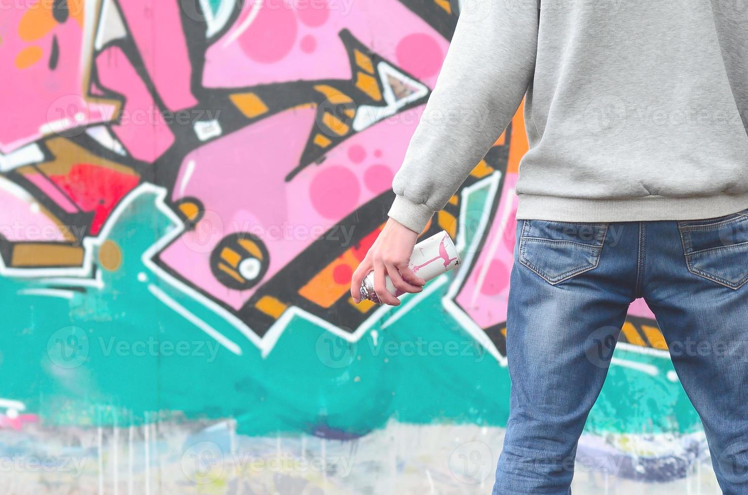 un jeune graffeur dans un sweat à capuche gris regarde le mur avec photo