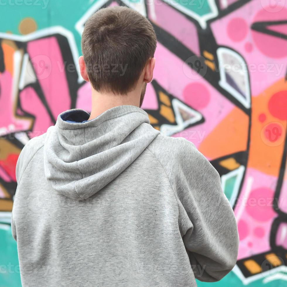 un jeune graffeur dans un sweat à capuche gris regarde le mur avec photo