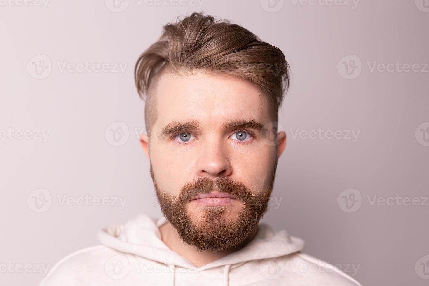 portrait de jeune homme avec barbe et moustache et coiffure à la mode. porte un sweat à capuche décontracté, a une expression sérieuse en studio sur fond blanc photo