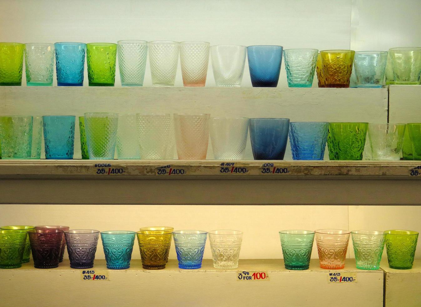 de nombreux verres d'eau colorés avec prix sur une étagère en bois blanc à vendre au magasin de céramique ou de vaisselle. groupe d'objets sur fond de bois photo