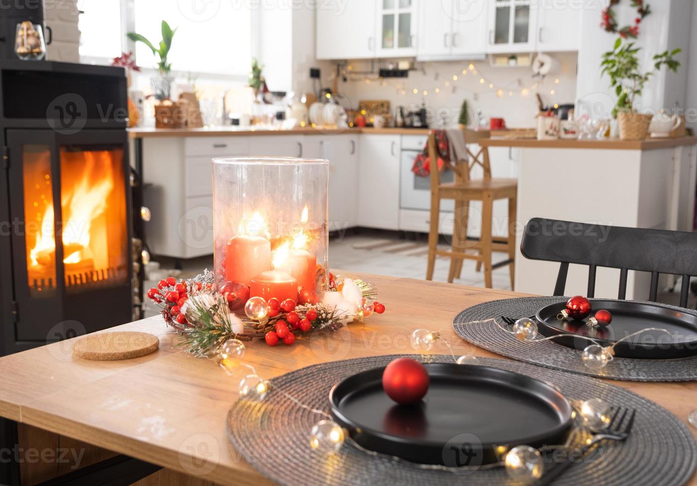 l'intérieur festif de la maison est décoré pour noël et le nouvel an dans un style loft avec poêle noir, cheminée, arbre de noël. chambre studio chaleureuse avec table dressée, feu de bois, cosy et chauffage d'accueil photo