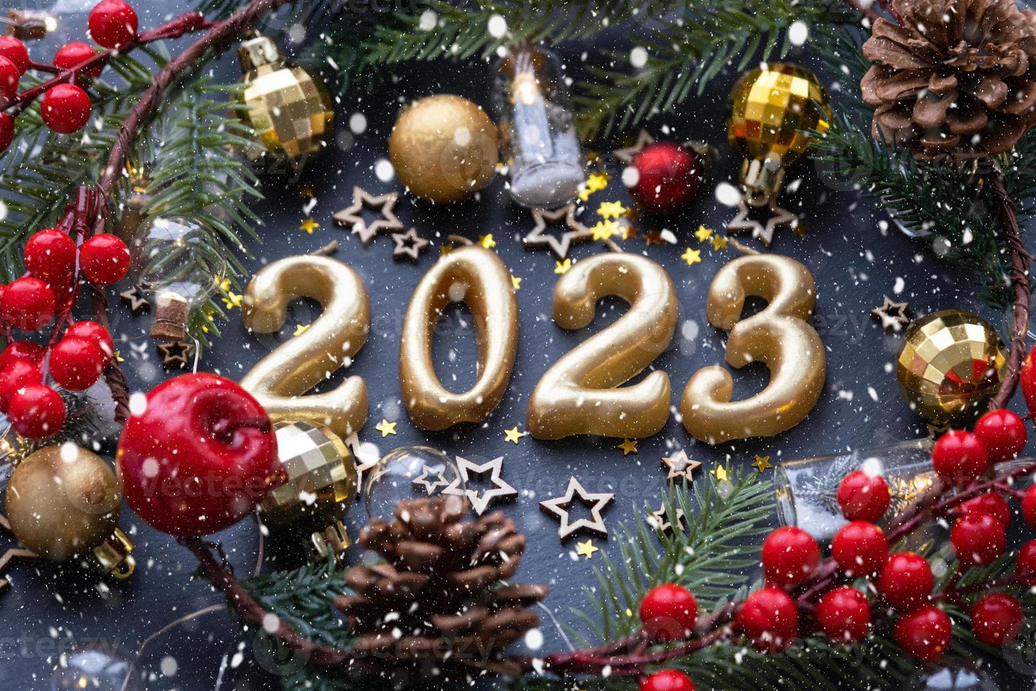 les figures dorées 2023 faites de bougies sur fond d'ardoise en pierre noire sont ornées d'un décor festif d'étoiles, de sequins, de branches de sapin, de boules et de guirlandes. carte de voeux, bonne année. photo