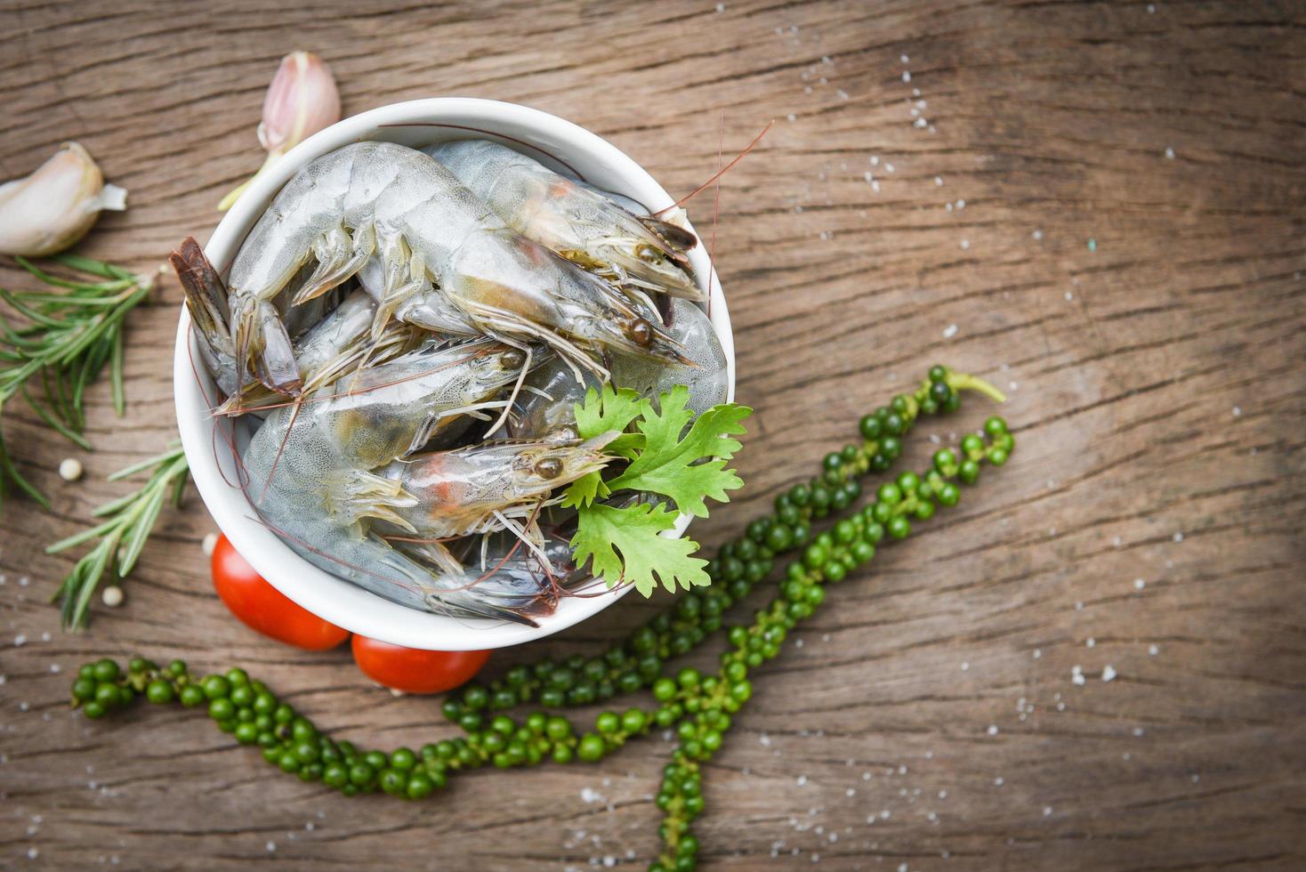 crevettes fraîches sur bol blanc et fond en bois avec ingrédients herbes et épices pour la cuisson des fruits de mer - crevettes crevettes crues photo