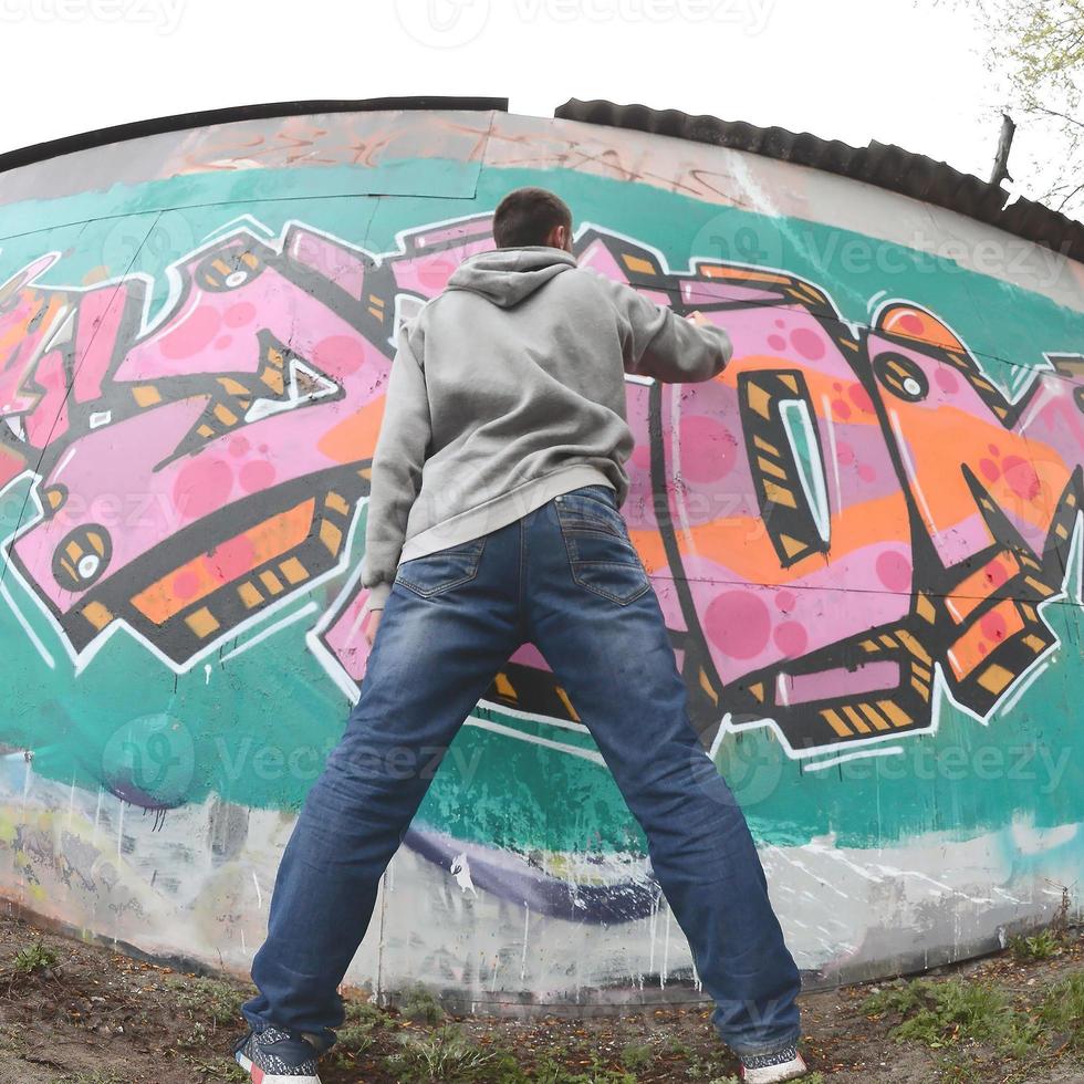 un jeune homme dans un sweat à capuche gris peint des graffitis en rose et vert c photo