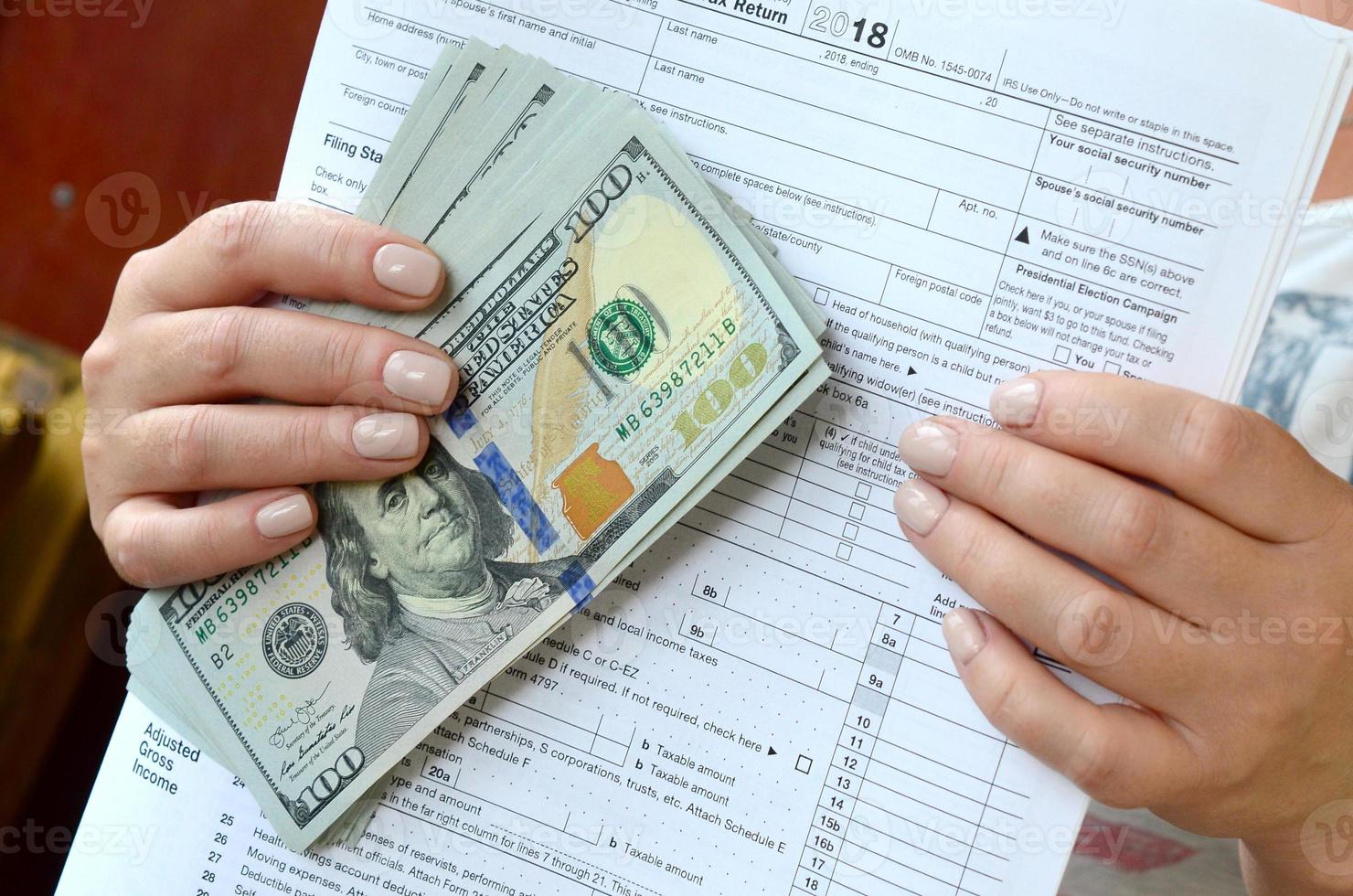 la jeune fille tient dans ses mains le formulaire fiscal et un grand nombre de billets d'un dollar photo