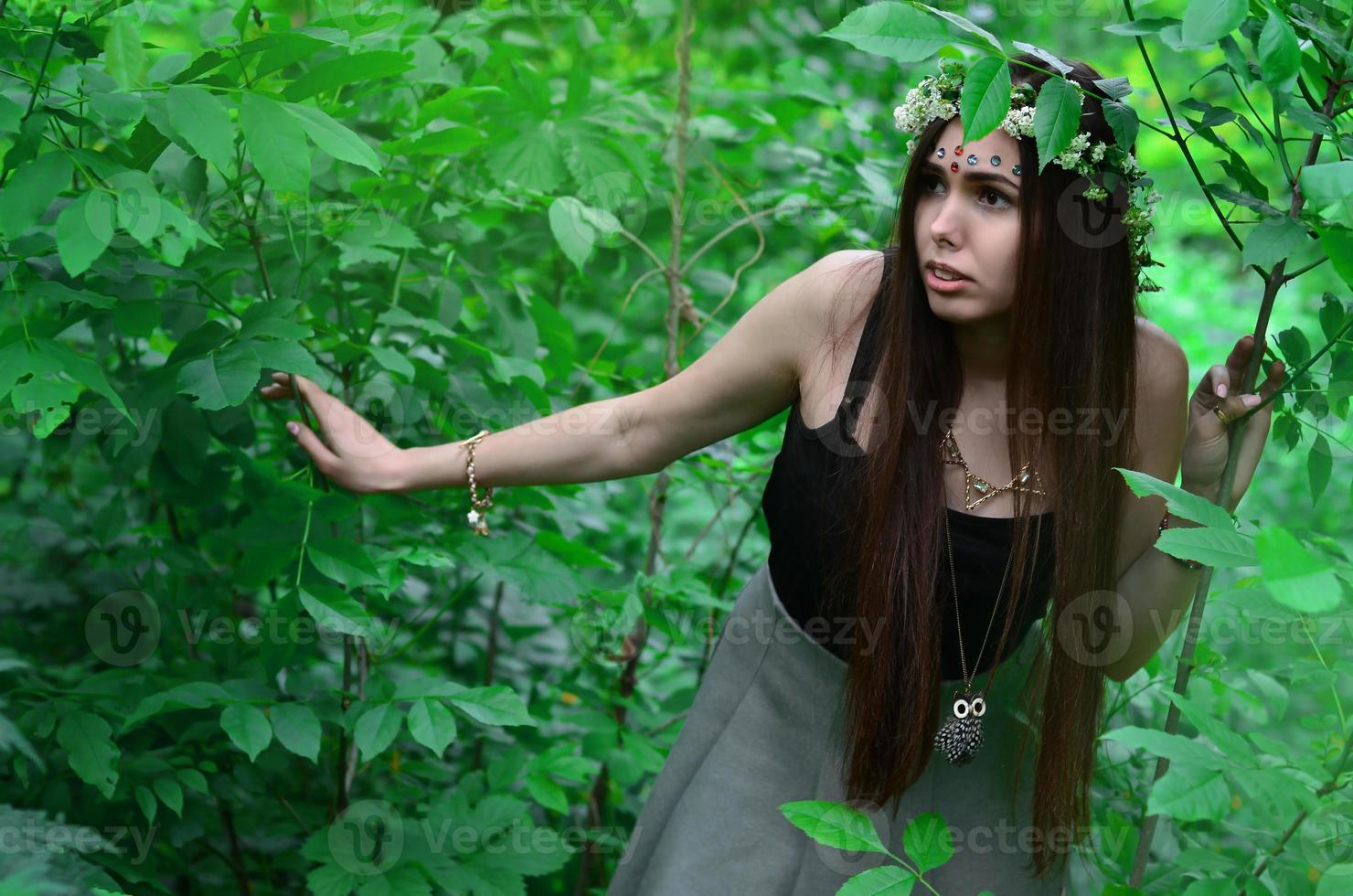 une photo de forêt d'une belle jeune brune d'apparence européenne aux yeux marron foncé et aux grandes lèvres. sur la tête de la jeune fille porte une couronne de fleurs, sur son front des décorations brillantes