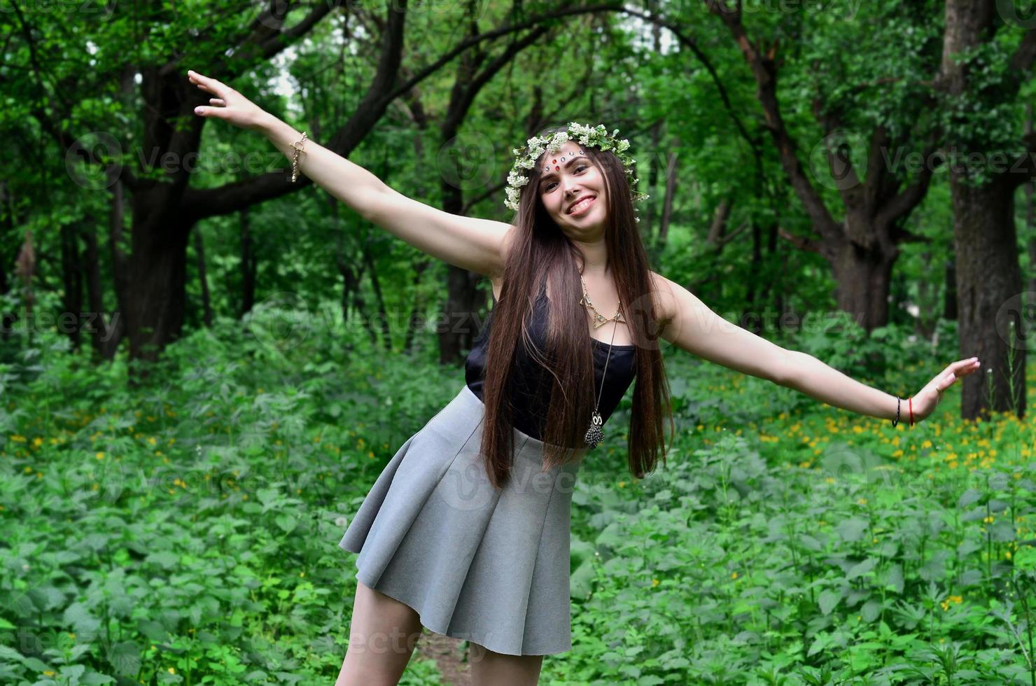 portrait d'une jeune fille émotive avec une couronne de fleurs sur la tête et des ornements brillants sur le front. jolie brune posant dans une belle forêt en plein essor pendant la journée par beau temps photo