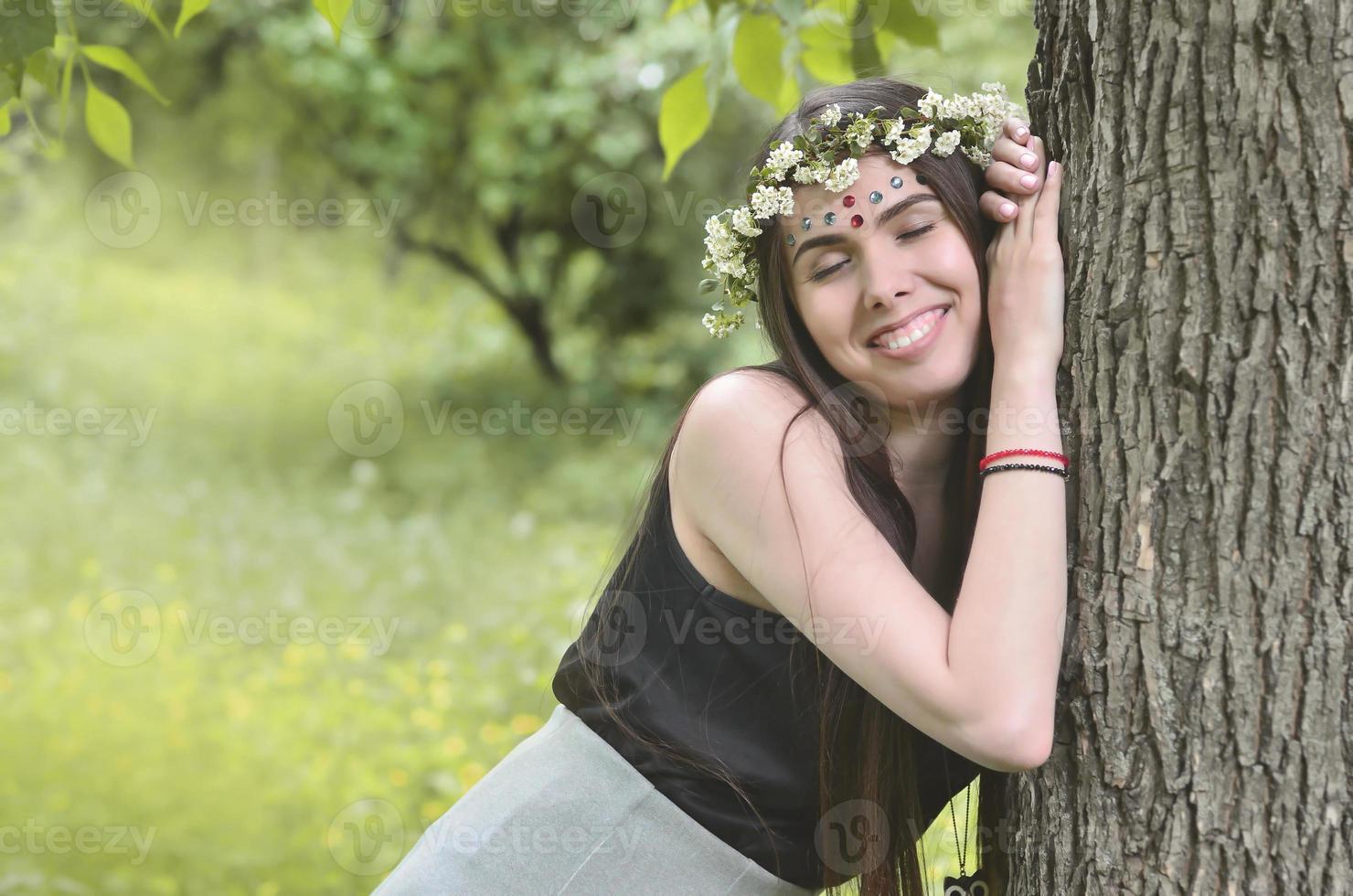 une photo de forêt d'une belle jeune brune d'apparence européenne aux yeux marron foncé et aux grandes lèvres. sur la tête de la jeune fille porte une couronne de fleurs, sur son front des décorations brillantes