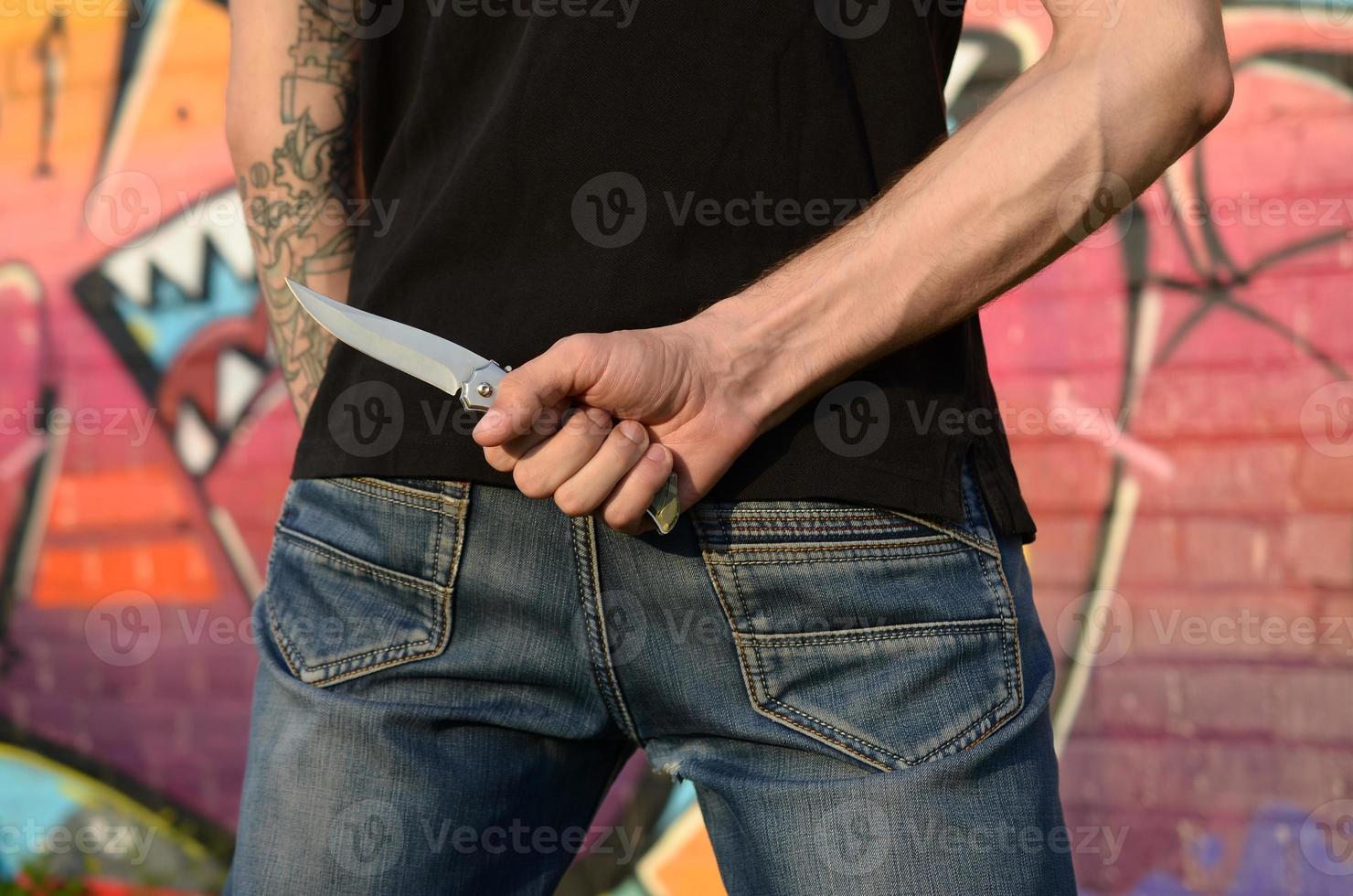 vue arrière du jeune homme de race blanche avec un couteau à la main contre le mur de briques du ghetto avec des graffitis. concept de forces criminelles et accusation d'agression photo