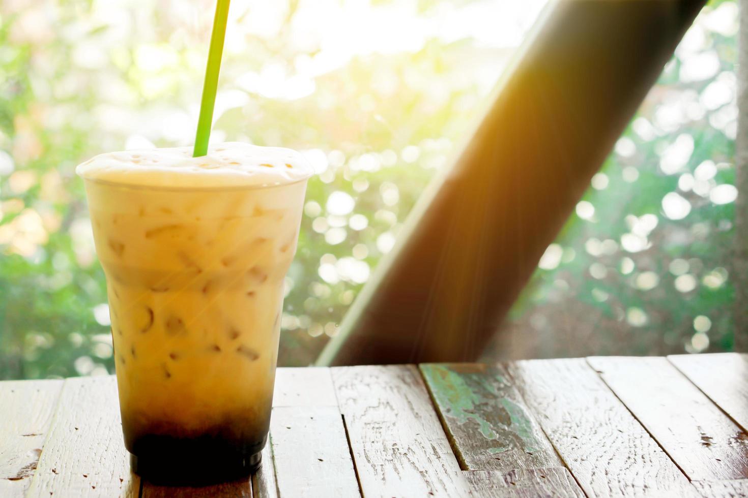latte de glace sur une terrasse en bois près du jardin avec éruption solaire et arrière-plan vert. le latte glacé est une boisson populaire en été en thaïlande. photo