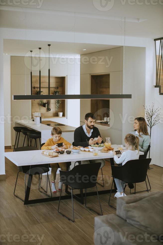 famille utilisant des téléphones portables tout en prenant son petit déjeuner à la table à manger de l'appartement photo