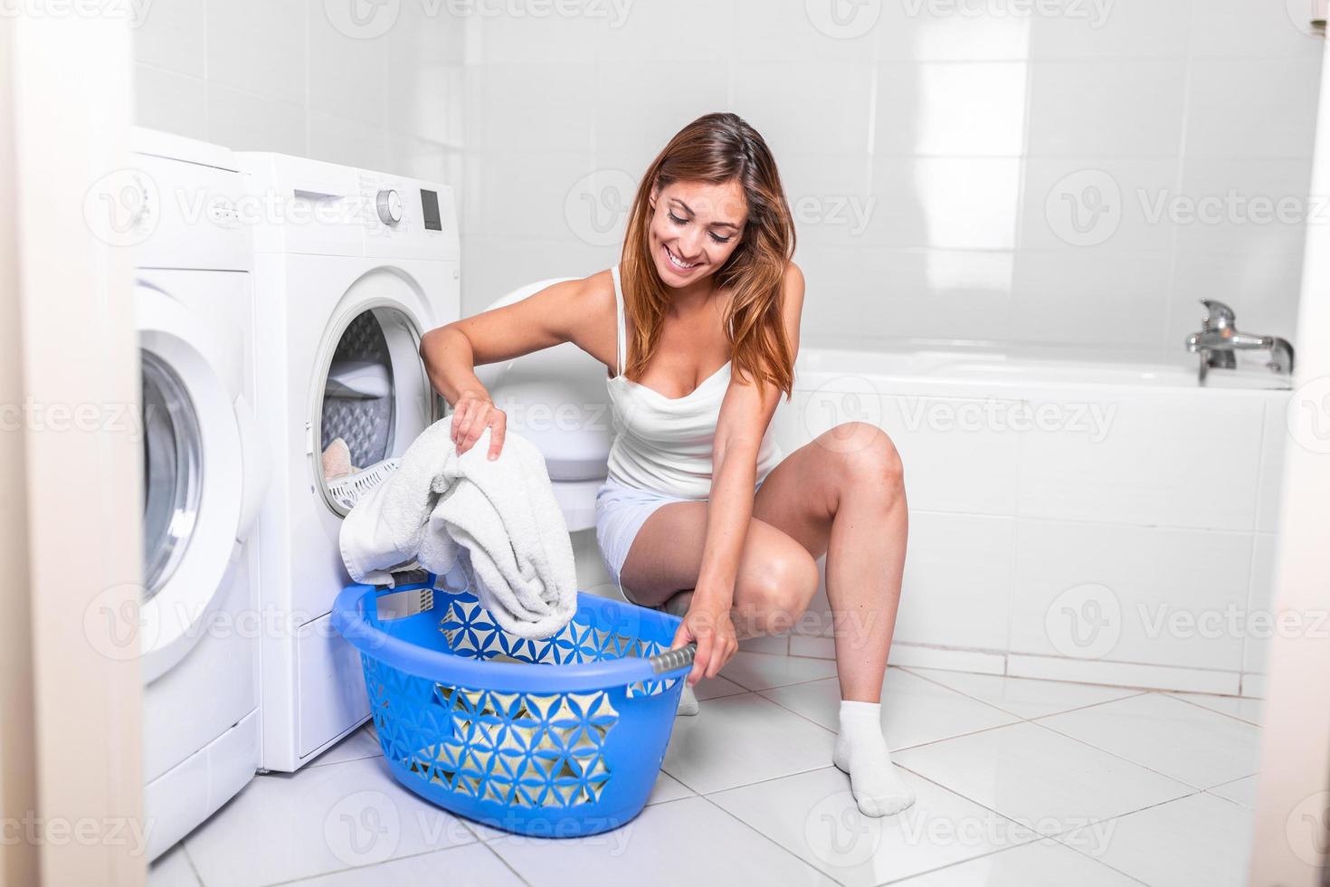 jeune femme sortant le linge de la machine à laver à la maison, gros plan d'une machine à laver chargée de vêtements, prenant à la main des serviettes de couleur photo