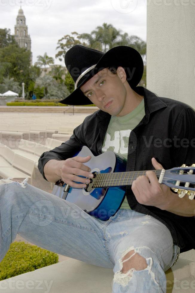 beau jeune cow-boy jouant de la guitare dans le parc. photo