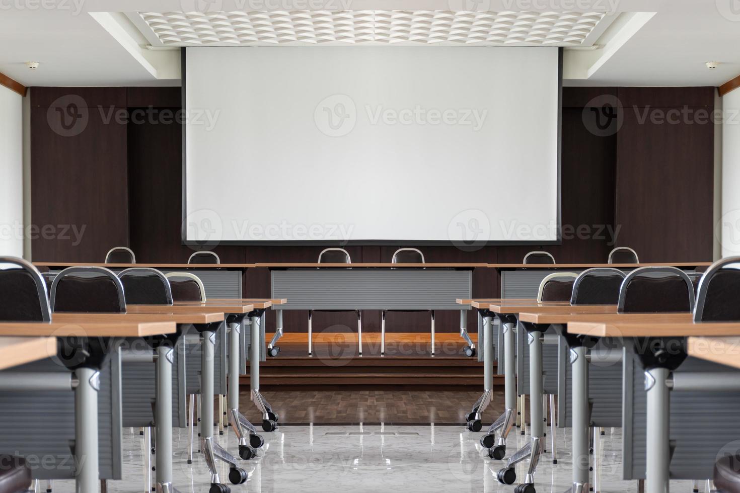 salle de séminaire avec une table d'orateur au milieu de la scène et un fond d'écran blanc photo