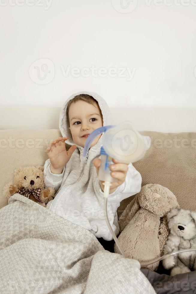 petit garçon malade avec inhalateur pour le traitement de la toux. enfant  malade faisant de l'inhalation sur son lit. saison de la grippe.  intervention médicale à domicile. intérieur et vêtements aux couleurs