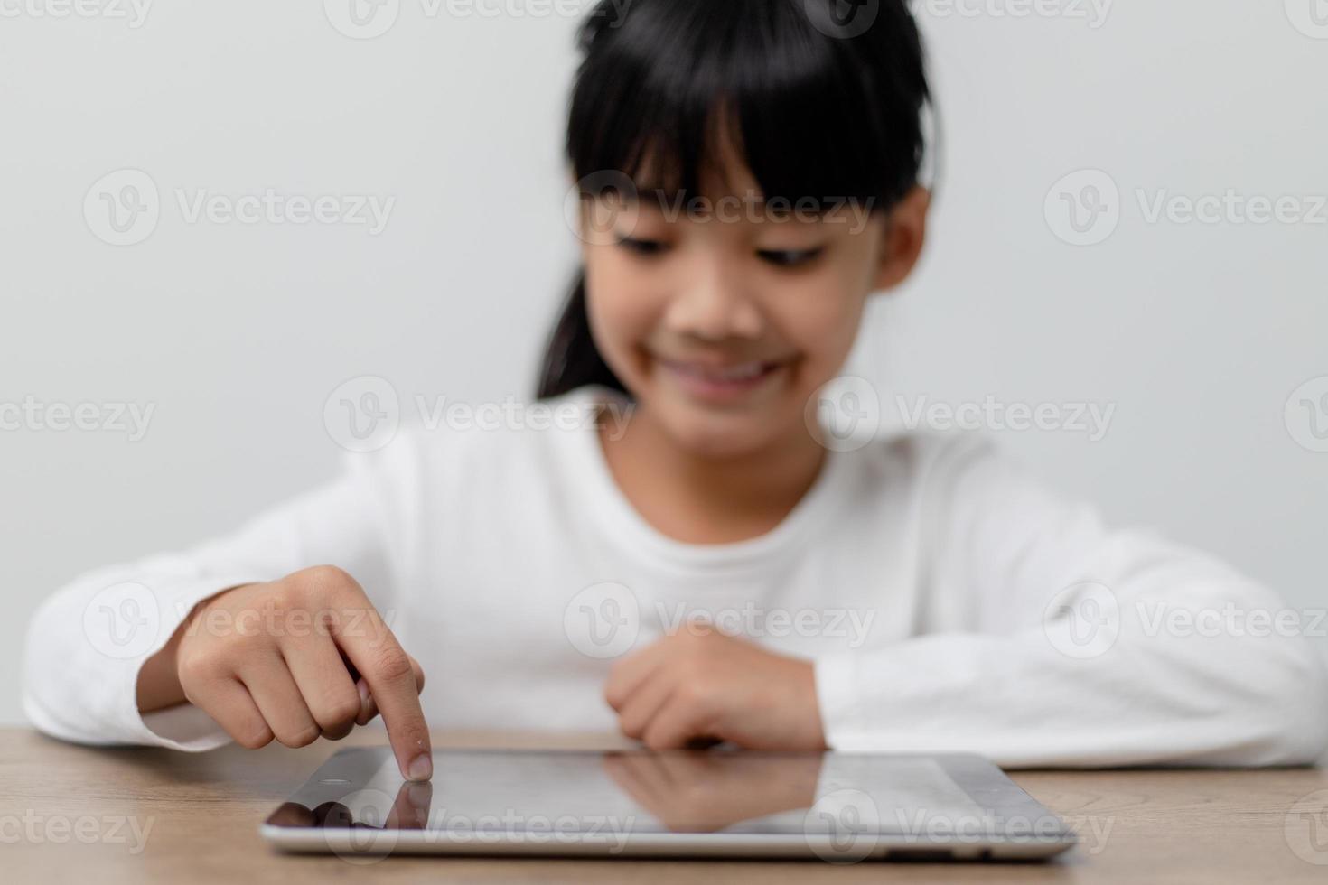 petite fille mignonne asiatique touchant l'écran de la tablette numérique sur la table photo