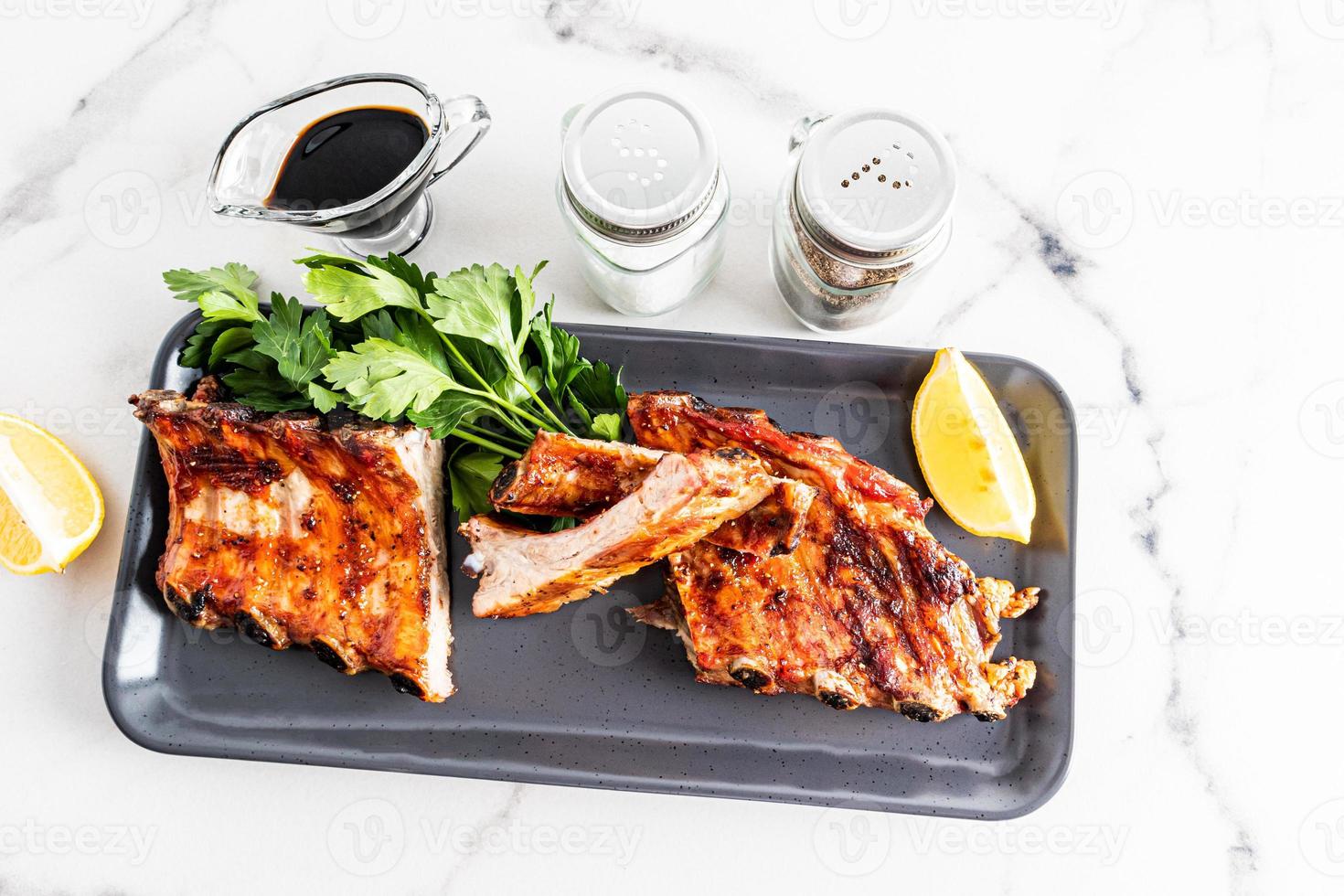 côtes de porc grillées sur un plateau en céramique sombre avec des ingrédients sur un fond factuel blanc. nourriture exquise pour les amateurs de barbecue. photo