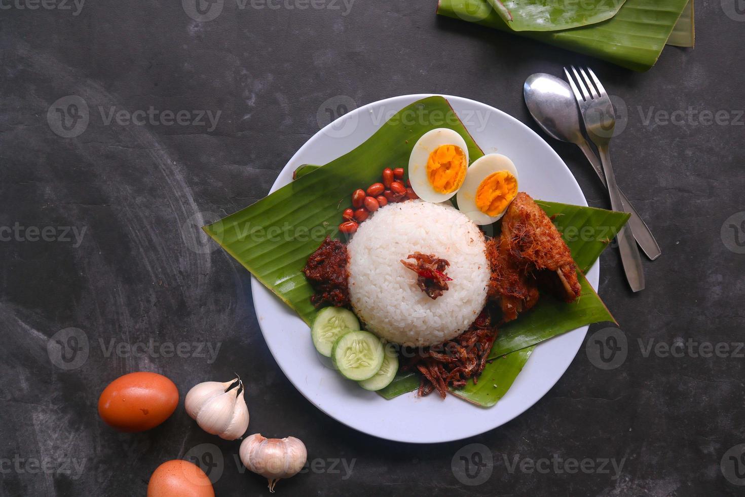 nasi lemak, est des œufs durs traditionnels malais, des haricots, des anchois, de la sauce chili, du concombre. du plat servi sur une feuille de bananier photo