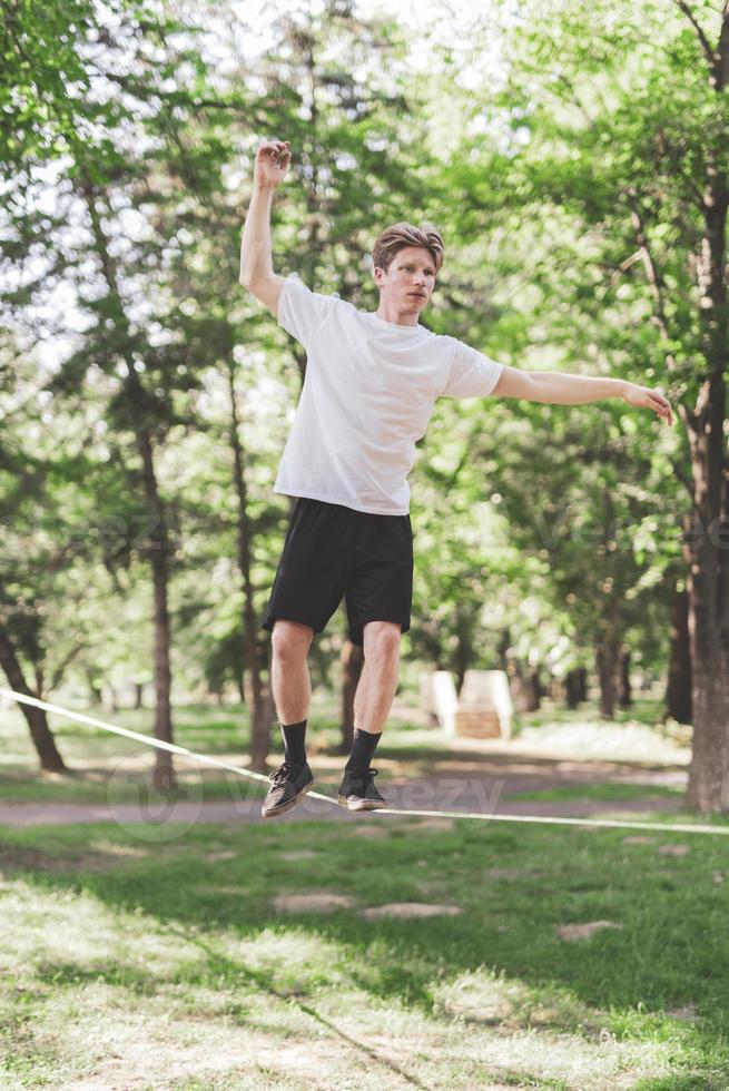 jeune homme équilibrant et sautant sur slackline. homme marchant, sautant et équilibrant sur une corde dans le parc. photo