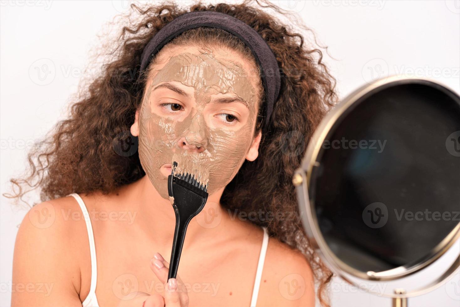 procédures de beauté concept de soins de la peau. jeune femme appliquant un masque facial d'argile de boue grise sur son visage photo