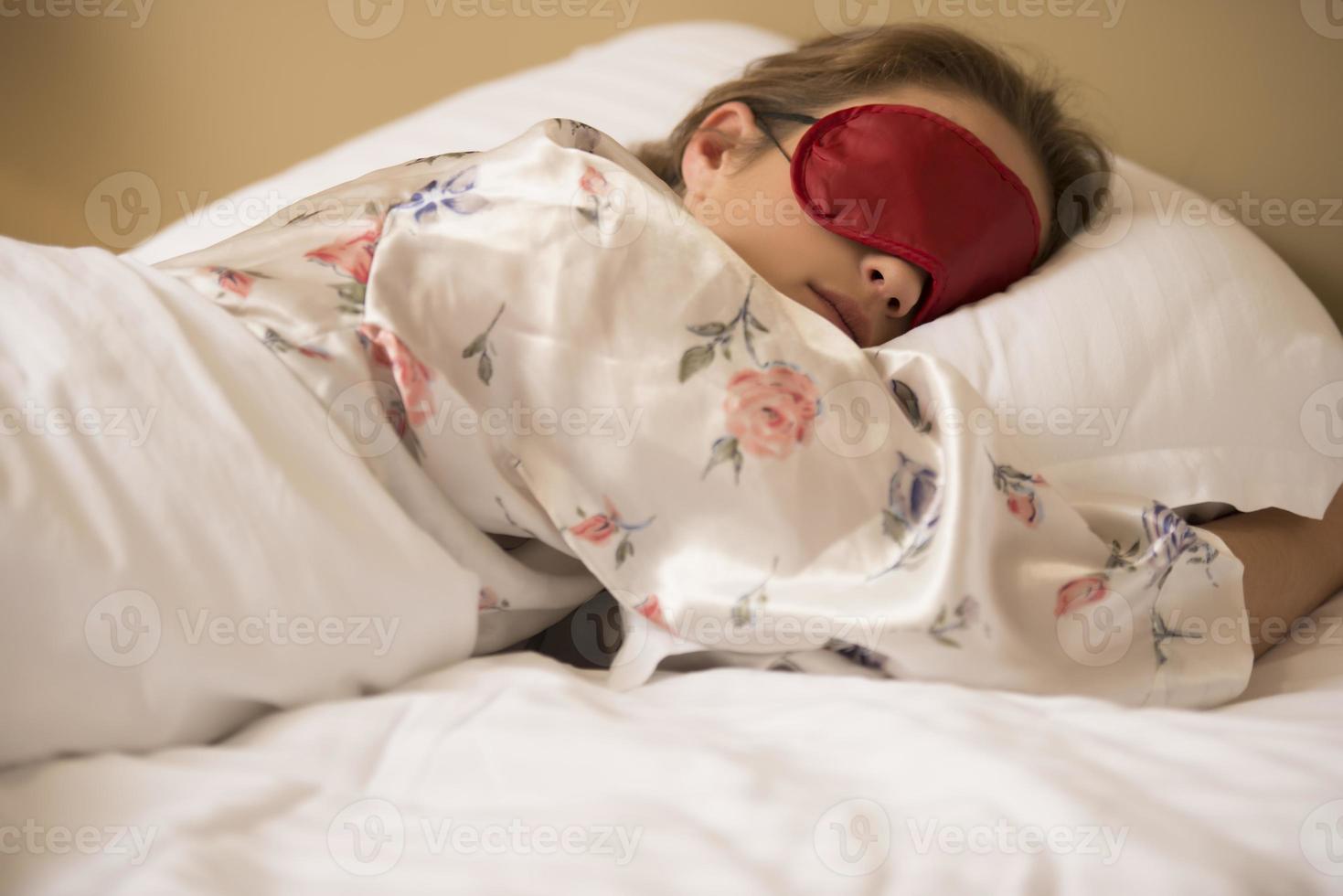 femme fatiguée dormant dans son lit portant un masque de sommeil avec les yeux bandés photo