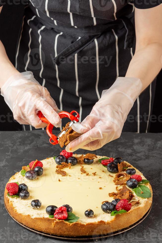 le chef féminin décore le gâteau au fromage classique fait maison avec des baies fraîches et du fromage salé râpé photo