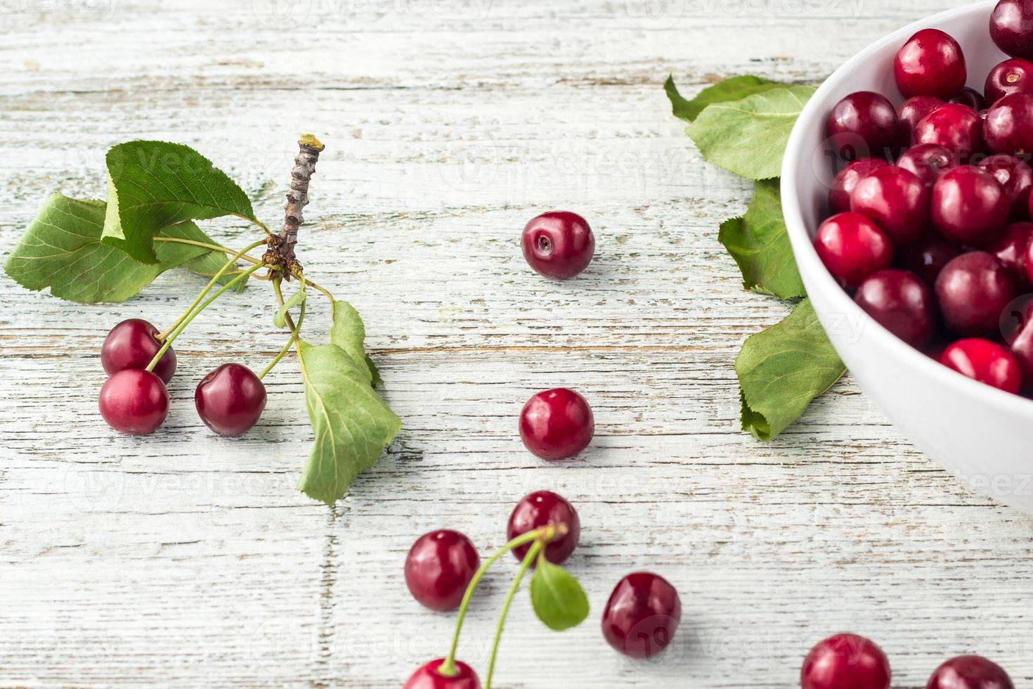 bol blanc de cerises douces fraîches avec des feuilles dans des gouttes d'eau sur fond de bois photo