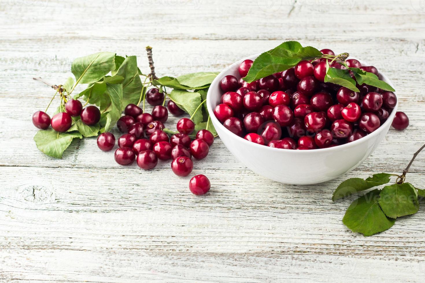 bol blanc de cerises douces fraîches avec des feuilles dans des gouttes d'eau sur fond de bois photo