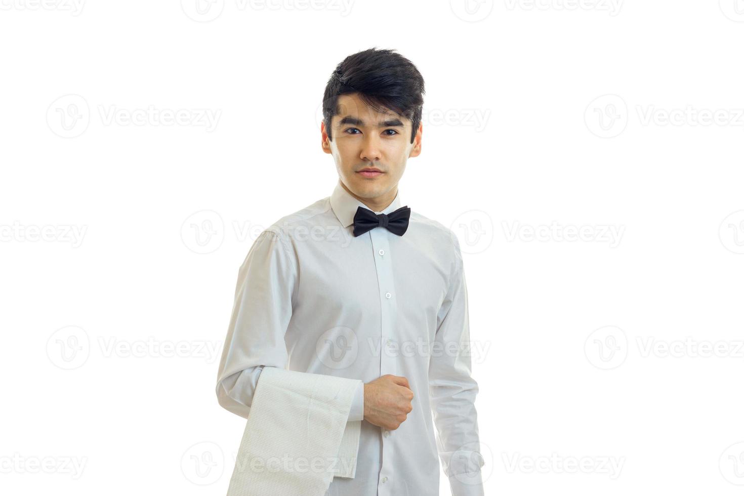 beau jeune serveur fort dans une chemise blanche avec un papillon a l'air droit et garde une serviette à portée de main photo