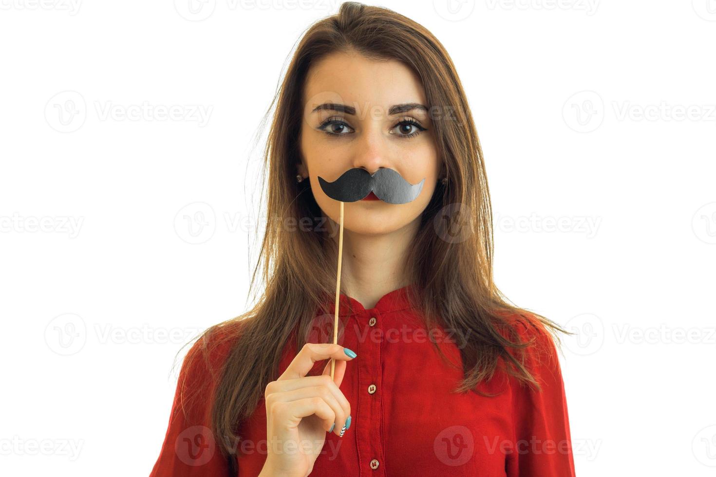 une jeune fille dans un chemisier rouge garde près de la bouche la moustache en papier est isolée sur fond blanc photo