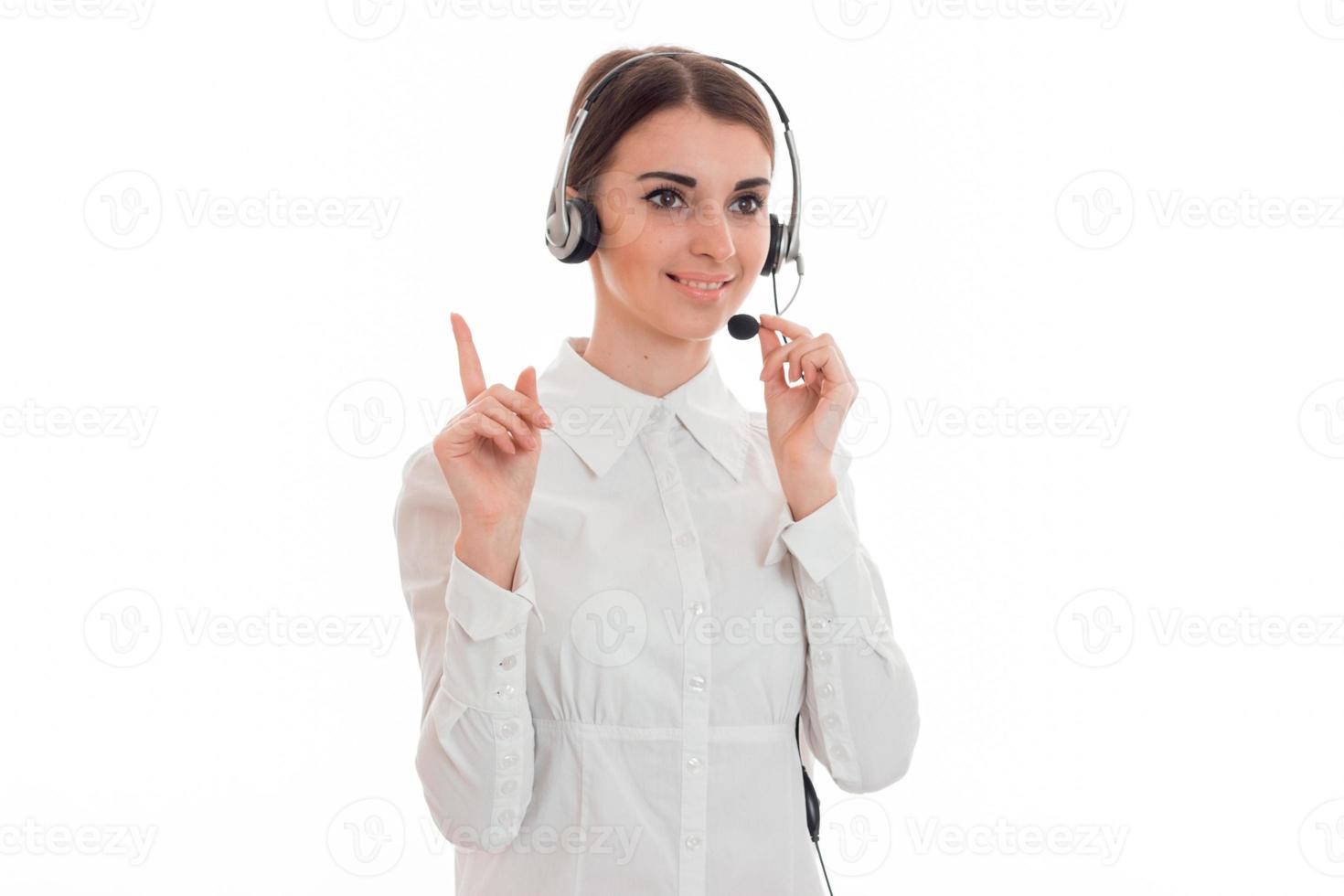 belle jeune fille dans un casque et une chemise blanche regarde de côté sourit et montre son doigt photo